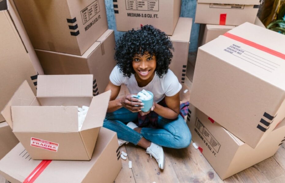 Woman surrounded by packing boxes, grinning and holding an undamaged mug full of packing foam
